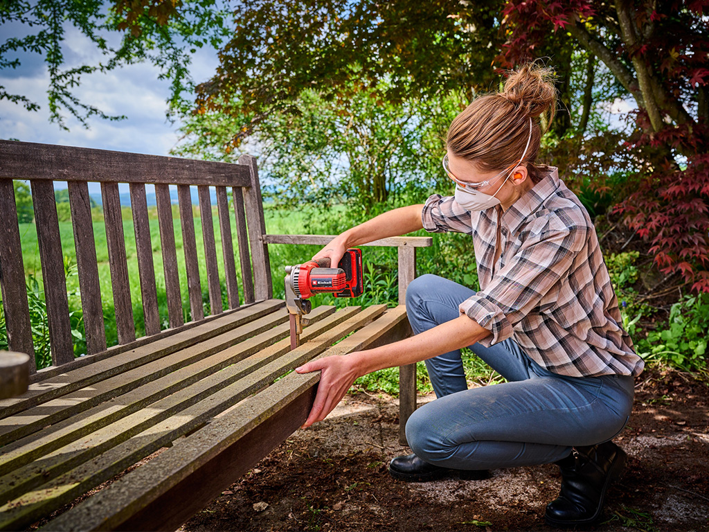 Woman in the garden sanding narrow gaps in a wooden garden bench with a cordless band file
